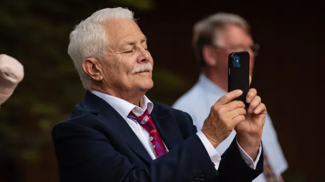 Elderly wedding guest capturing cherished moment at wedding, contributing to collecting wedding photos from guests