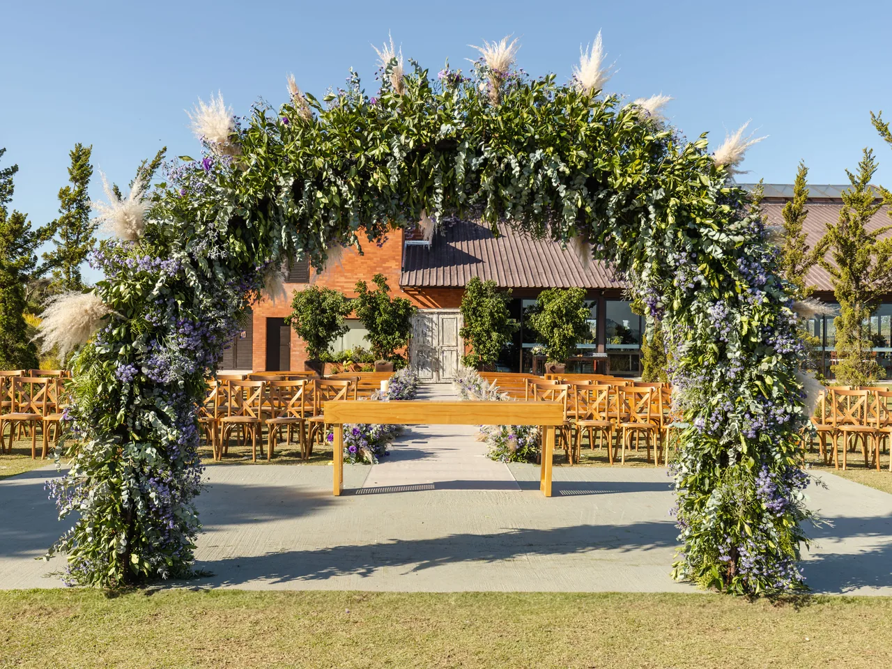 An outdoor wedding ceremony space with a flower arch and wooden chairs